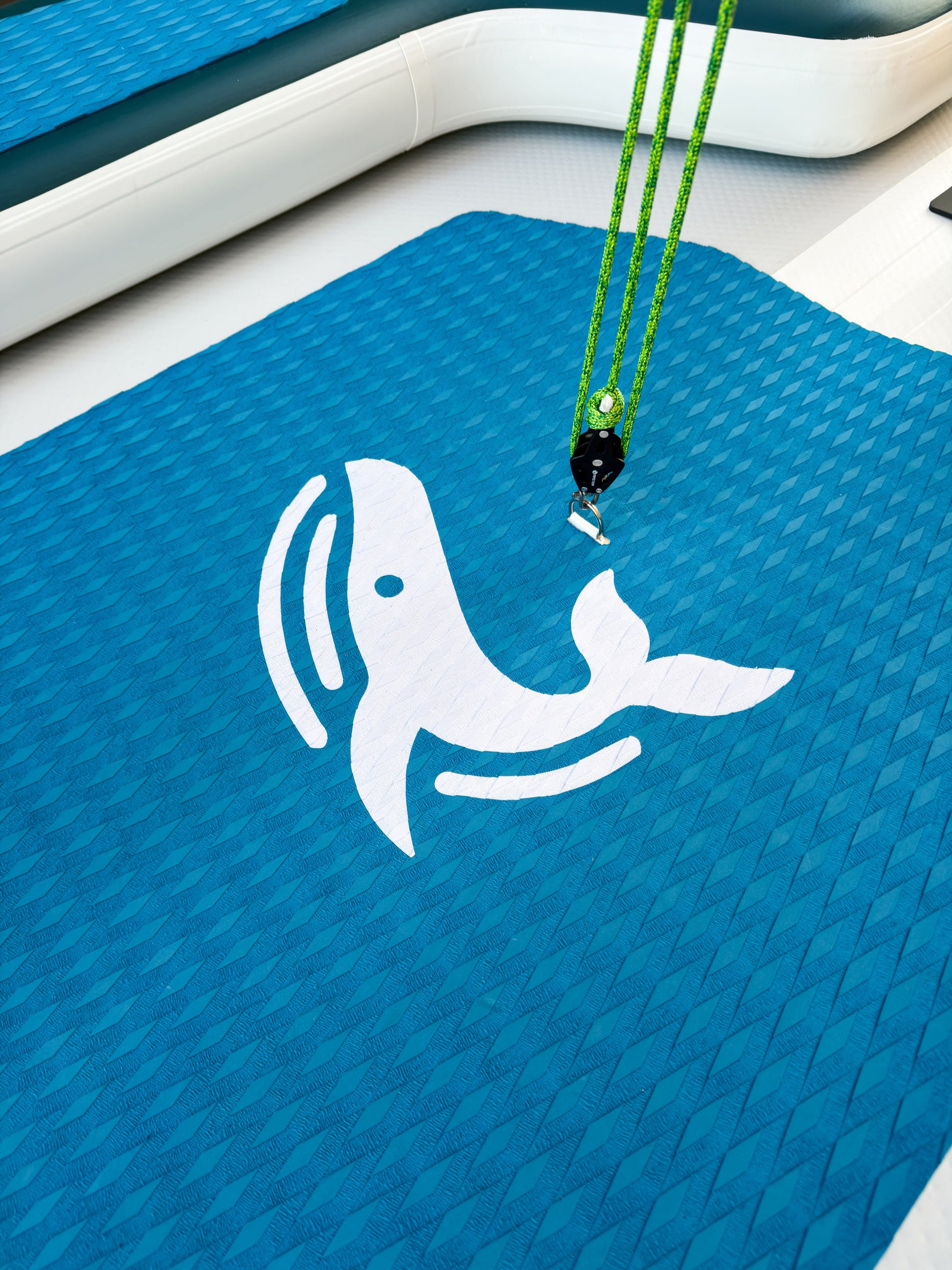 Blue mat with a white whale design and green lanyard on a boat deck.
