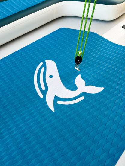 Blue mat with a white whale design and green lanyard on a boat deck.