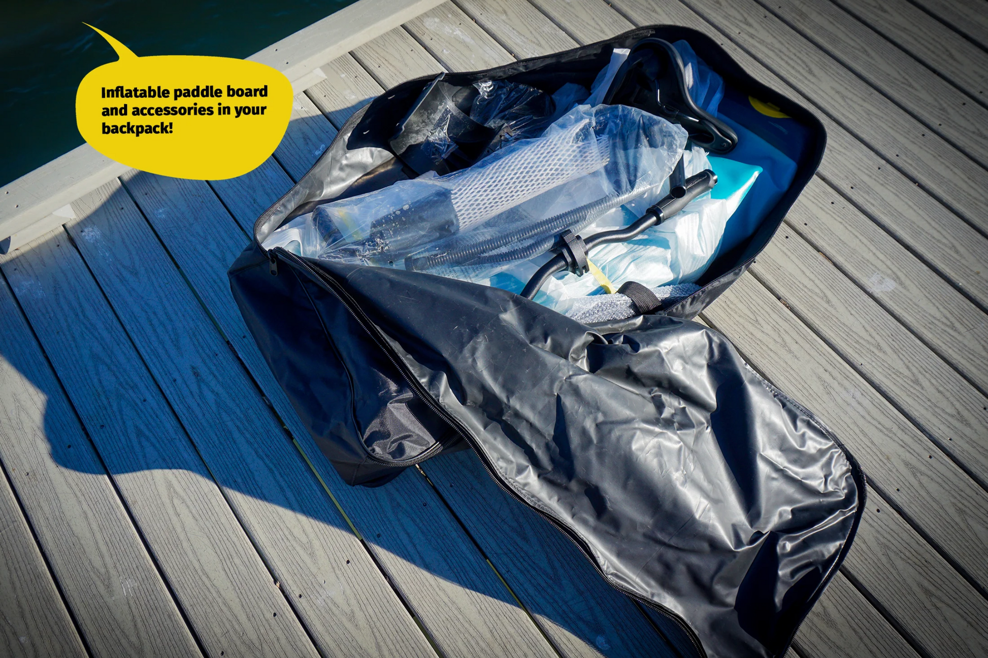 Inflatable paddle board and accessories in a backpack on a wooden deck.